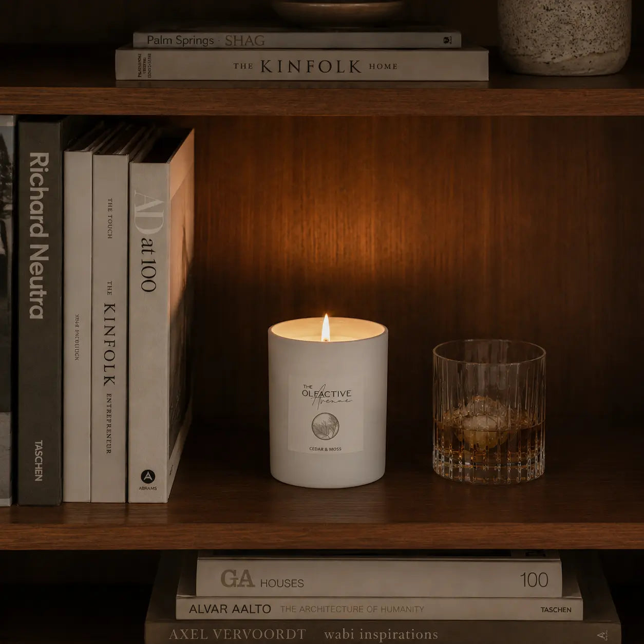 Duftkerze Cedar & Moss von The Olfactive Avenue — Kerzenlicht im Regal mit Büchern