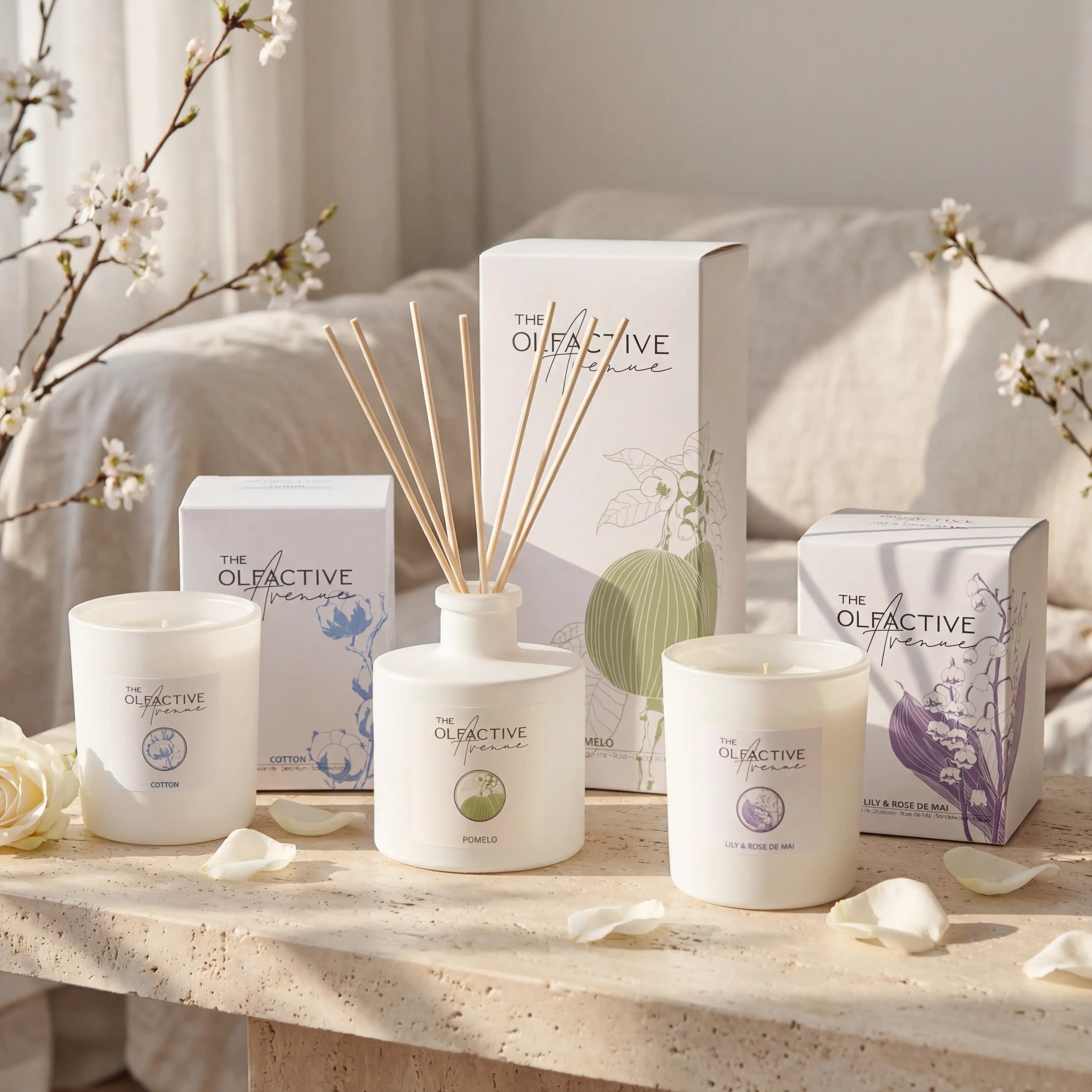 Luxuriöses Frühlings-Bundle von The Olfactive Avenue (TOA) bestehend aus den handgegossenen Duftkerzen Cotton und Lily & Rose de Mai sowie dem Pomelo Raumduft-Diffuser, arrangiert auf hellem Naturstein in warmem Frühlingslicht.