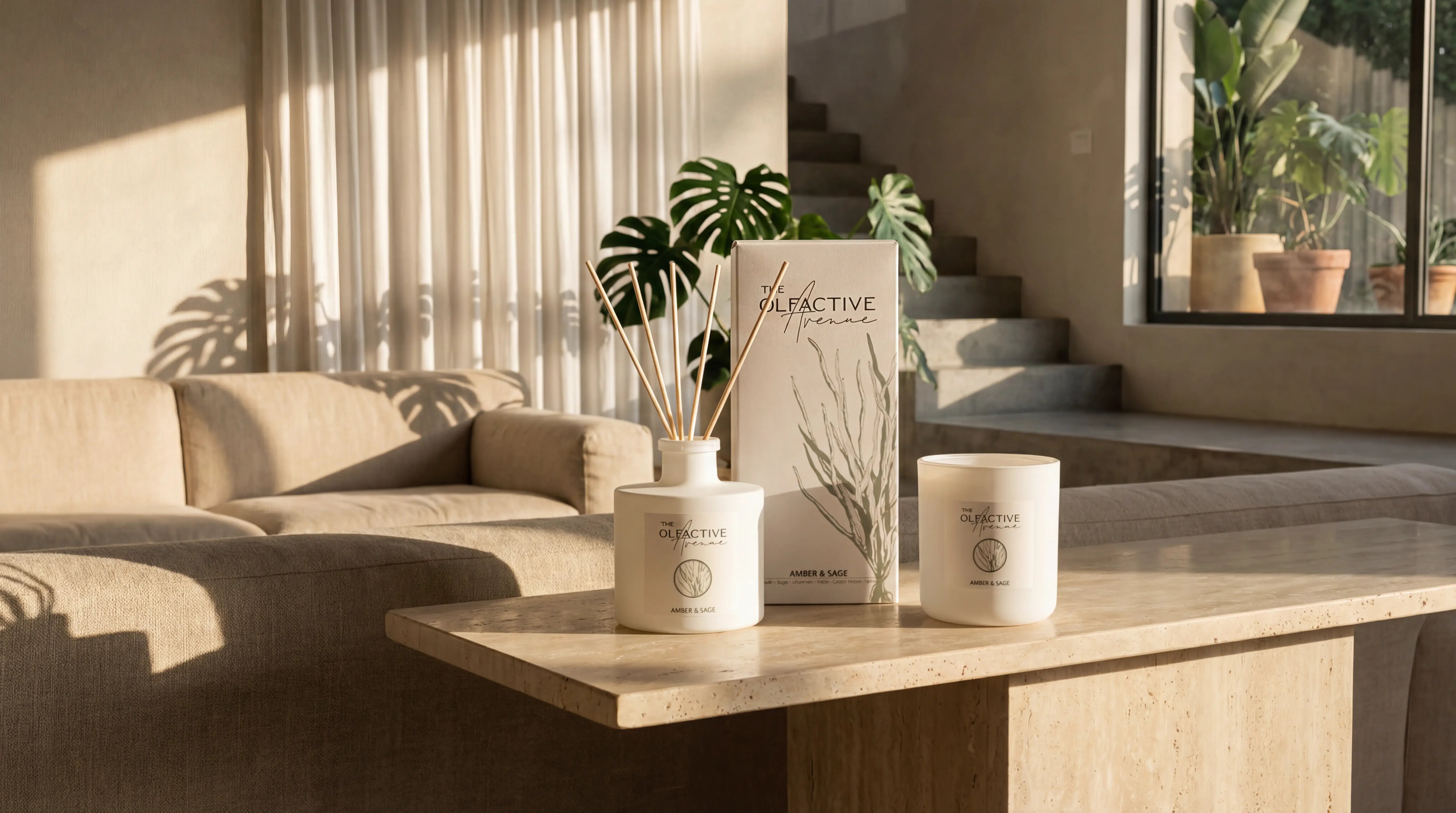 Die vollständige Amber & Sage Kollektion von The Olfactive Avenue, bestehend aus einem Raumduft-Diffuser, der passenden Design-Verpackung und einer matten Duftkerze, arrangiert in einem lichtdurchfluteten, minimalistischen Designer-Ambiente.
