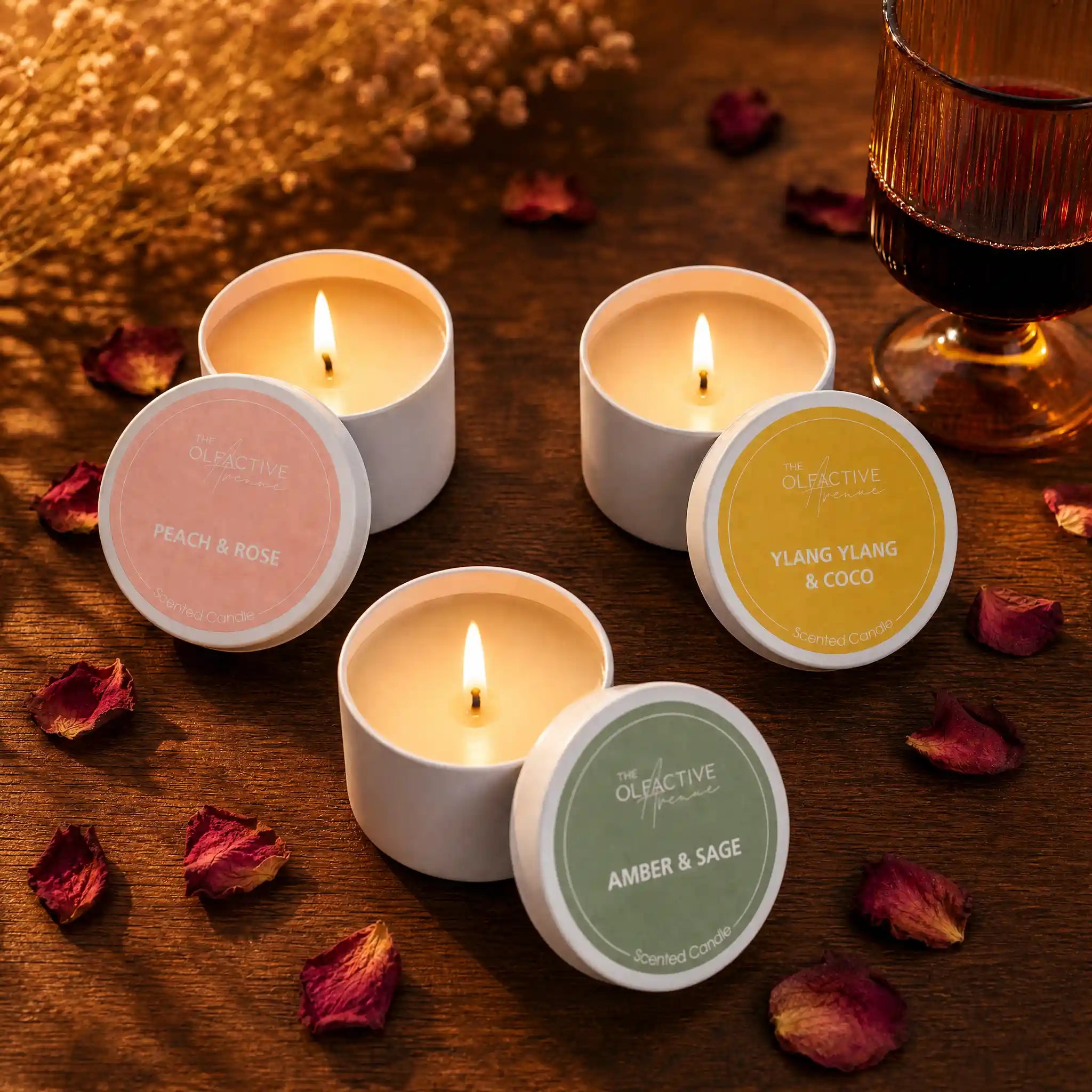 Brennende Travel Candles von The Olfactive Avenue mit Peach & Rose, Ylang Ylang & Coco und Amber & Sage auf warmem Holz mit Rosenblättern. Das Duftkerzen Bundle steht für sinnliche Abendrituale, gemütliche Atmosphäre und hochwertige Raumdüfte im kleinen Format.
