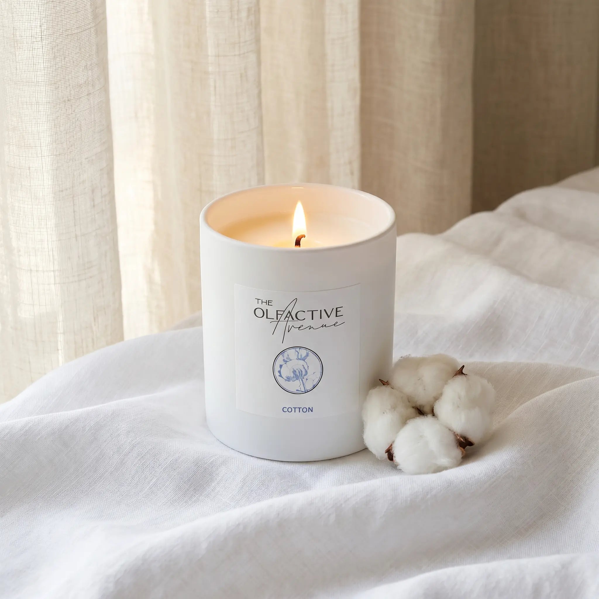 Duftkerze Cotton von The Olfactive Avenue auf weißem Leinen mit Baumwollblüte – Atmosphère Balance. [KI]