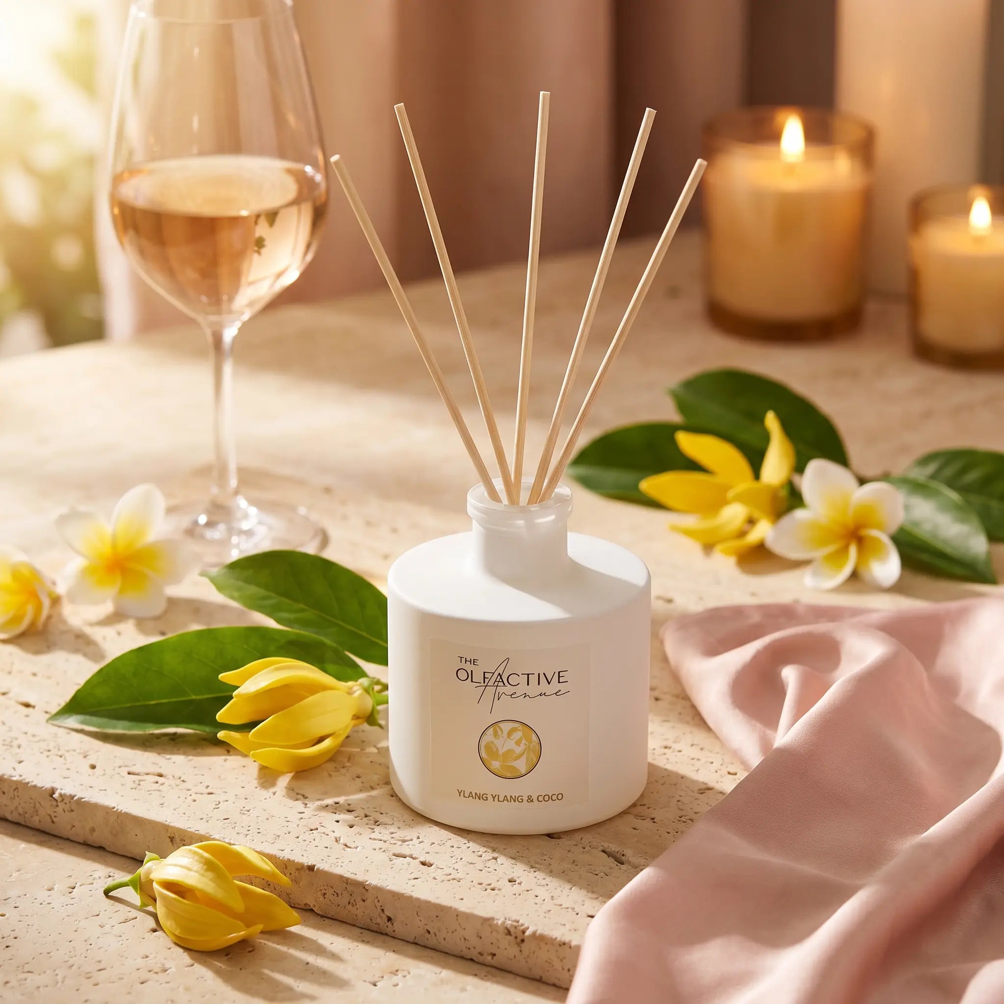 Raumduft Ylang Ylang & Coco von The Olfactive Avenue auf Travertin mit Rosé-Weinglas, Ylang-Ylang-Blüten und Plumeria im Sonnenuntergang – Atmosphère Sinnlich & Warm. [KI]