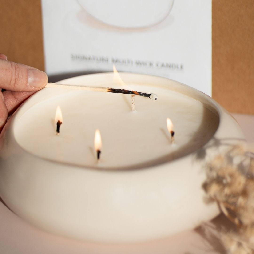 Nahaufnahme: Ein Streichholz entzündet die Dochte einer großen Duftkerze für ein entspannendes Selfcare-Ritual im Wohnzimmer.