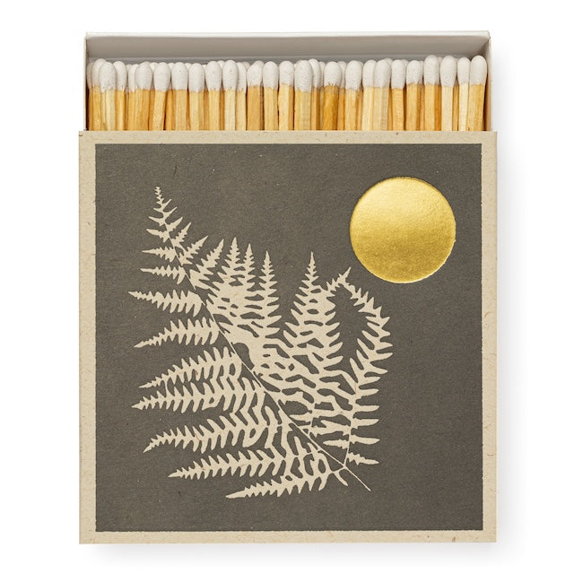 Quadratische Matchbox „Fern & Sun“: Farn-Illustration auf dunklem Fond mit goldener Sonne; 125 lange Streichhölzer, natur mit weißen Köpfen.