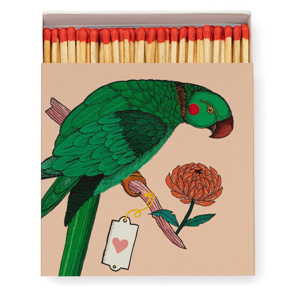 Quadratische Matchbox „Parrot“ von Archivist: grüner Papagei auf rosé; 125 lange Streichhölzer, natur mit roten Köpfen, weißes Tray.