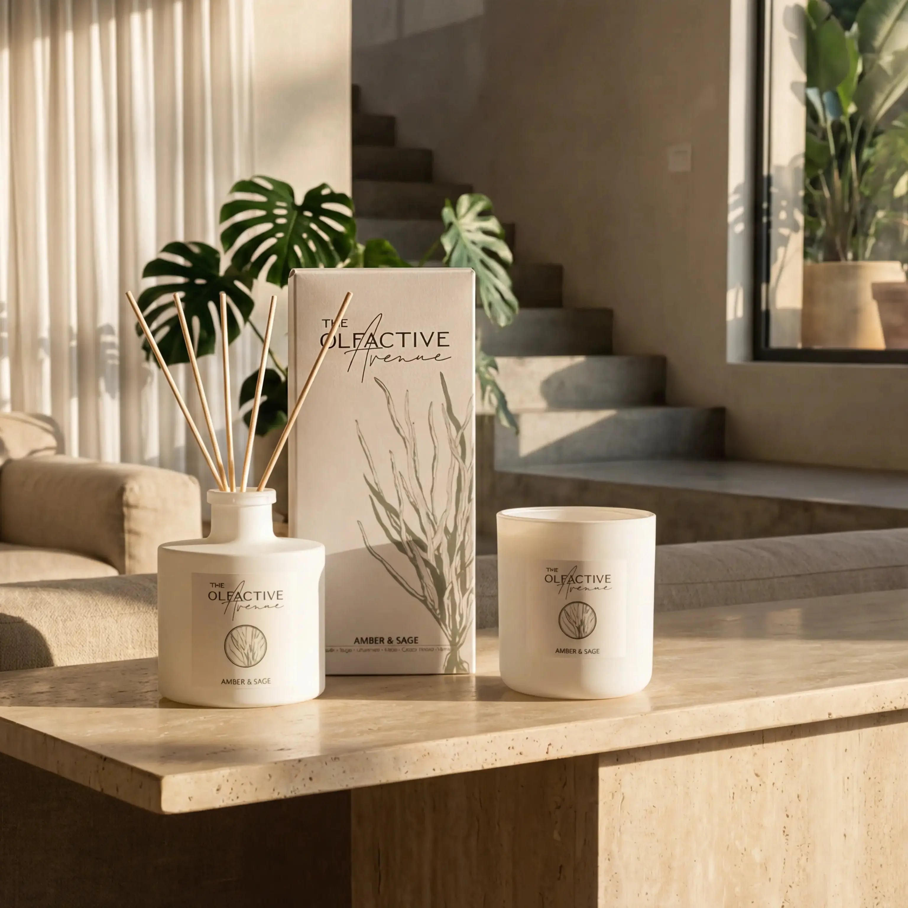Die vollständige Amber & Sage Kollektion von The Olfactive Avenue, bestehend aus einem Raumduft-Diffuser, der passenden Design-Verpackung und einer matten Duftkerze, arrangiert in einem lichtdurchfluteten, minimalistischen skandinavischen Designer-Ambiente.