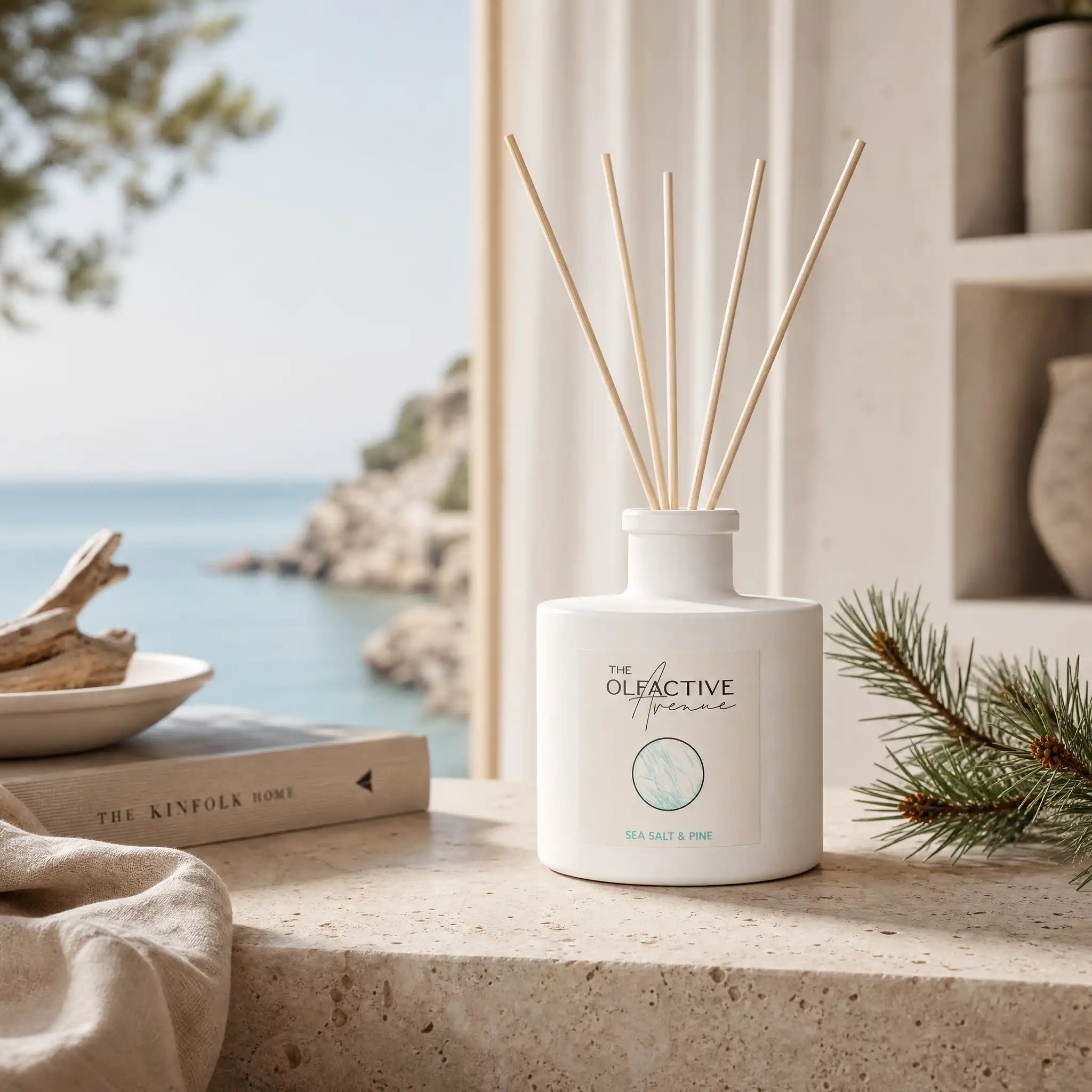 Sea Salt & Pine Duftstäbchen von The Olfactive Avenue vor einem Fenster mit Meerblick, Pinienzweig und Treibholz. [KI]