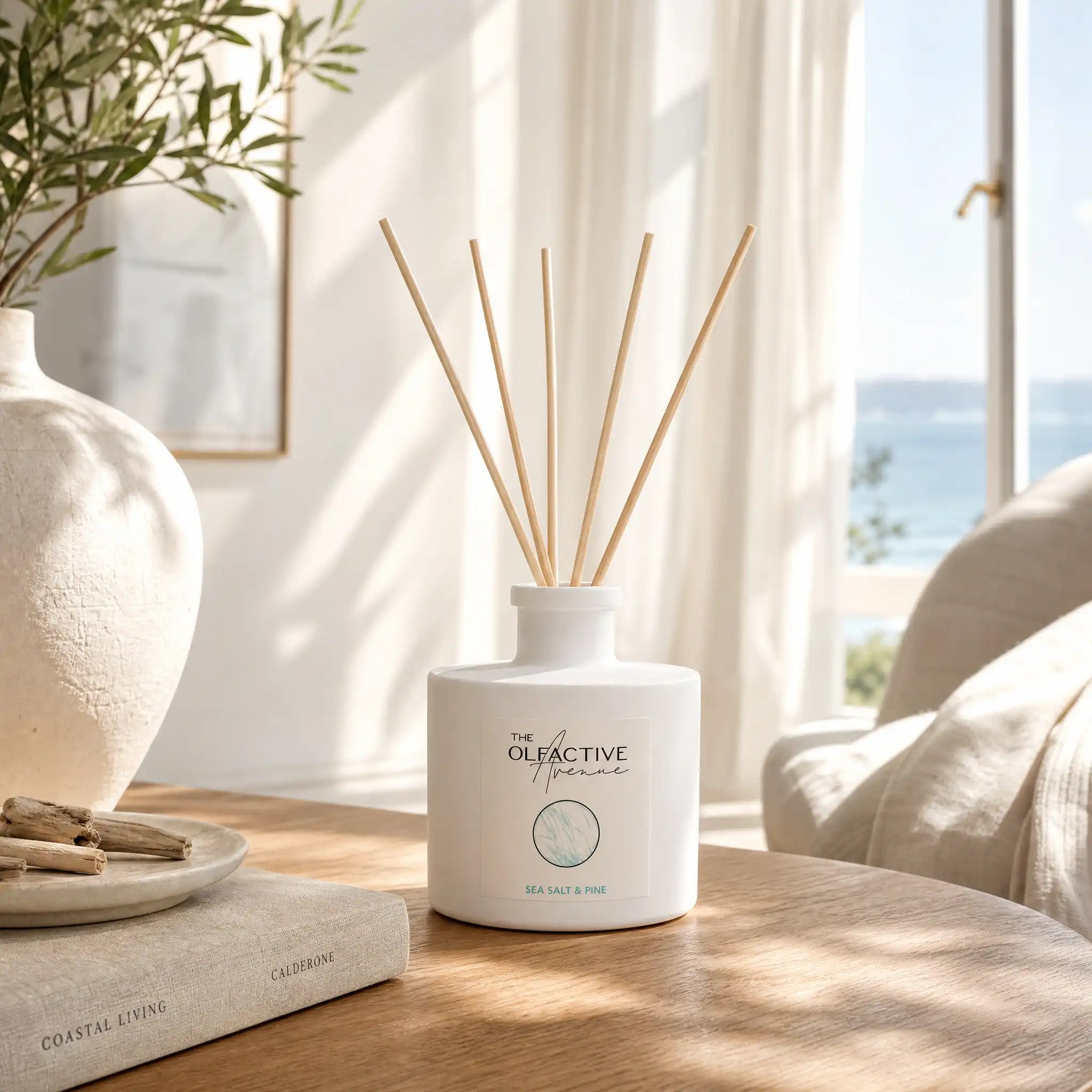 Sea Salt & Pine Raumdiffuser von The Olfactive Avenue auf einem Holztisch in einem sonnigen Küsteninterior mit Meerblick. [KI]