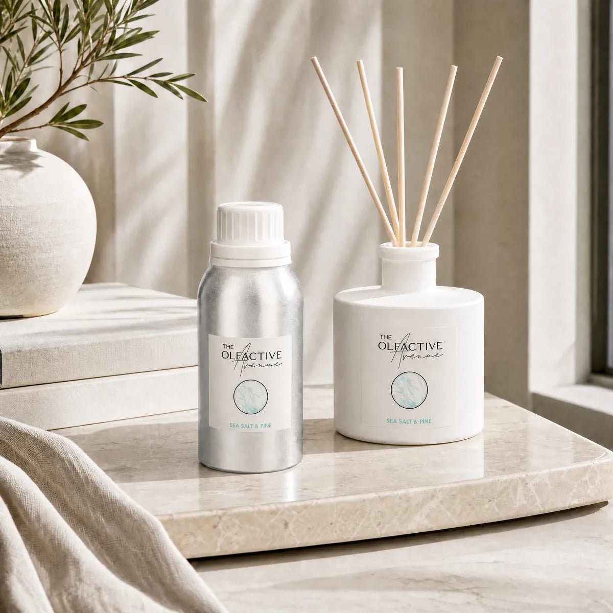 Verwöhn-Set von The Olfactive Avenue mit Raumduft-Diffuser und Nachfüll-Refill Sea Salt & Pine auf heller Marmorablage mit Olivenzweig [KI]