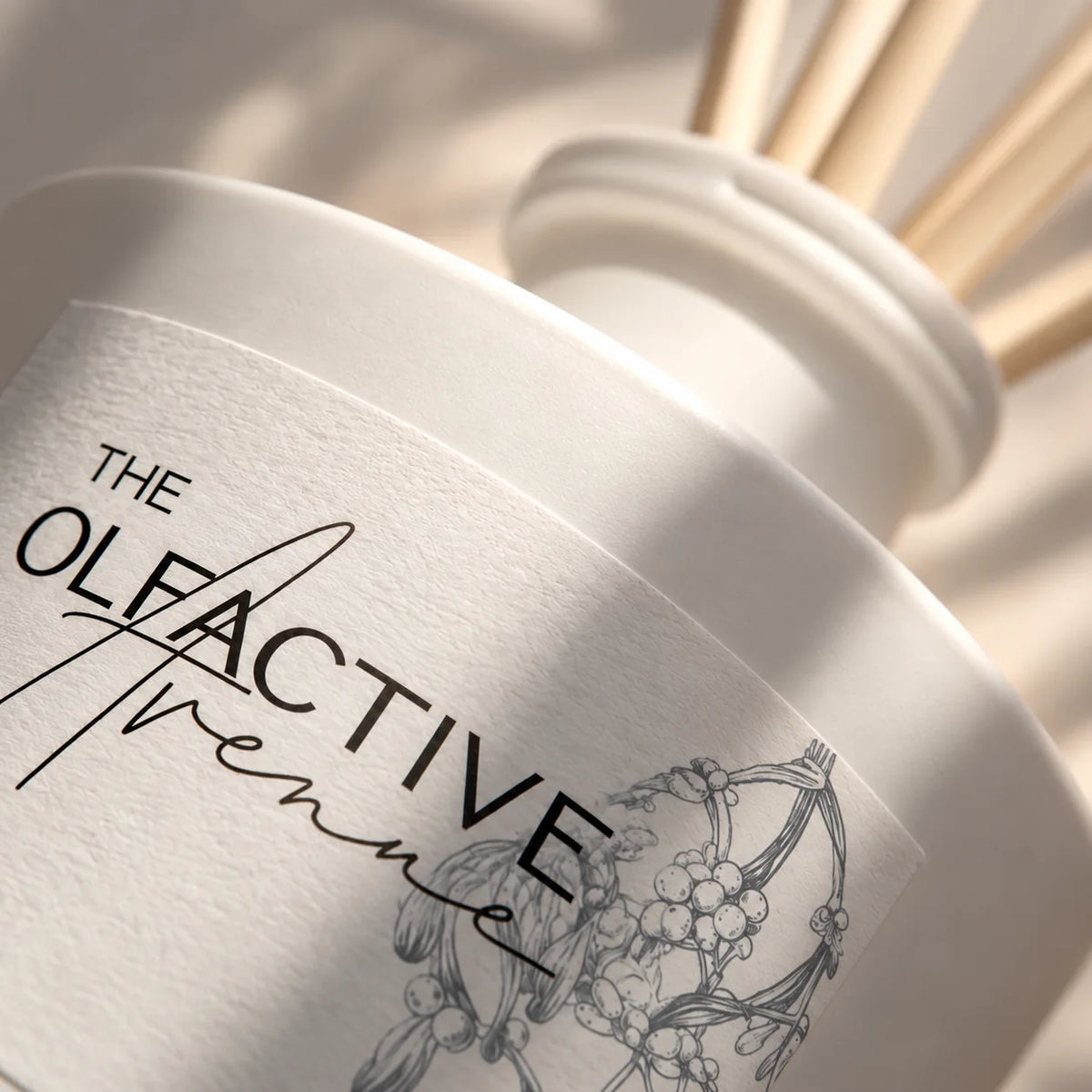 Detail des Etiketts vom Raumduft Winter Society von The Olfactive Avenue mit Logo und Mistelzweig-Illustration, weißer Flakon mit Rattanstäbchen [KI]